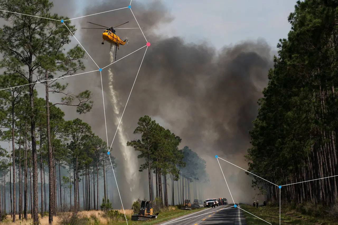 A helicopter dropping water on a forest fire beside a road.